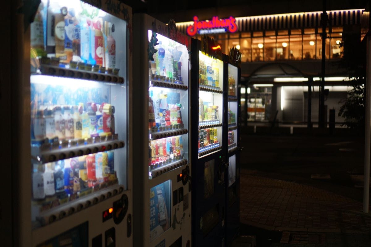 Rows of illuminated vending machines lining a narrow street at night in a Japanese city